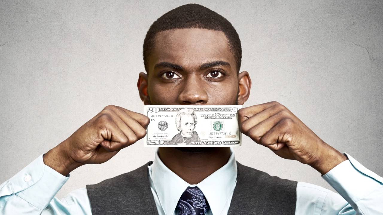 Homem negro com segurando uma nota de dolar em frente a sua boca, imagem usada no artigo queremos te ajudar a investir